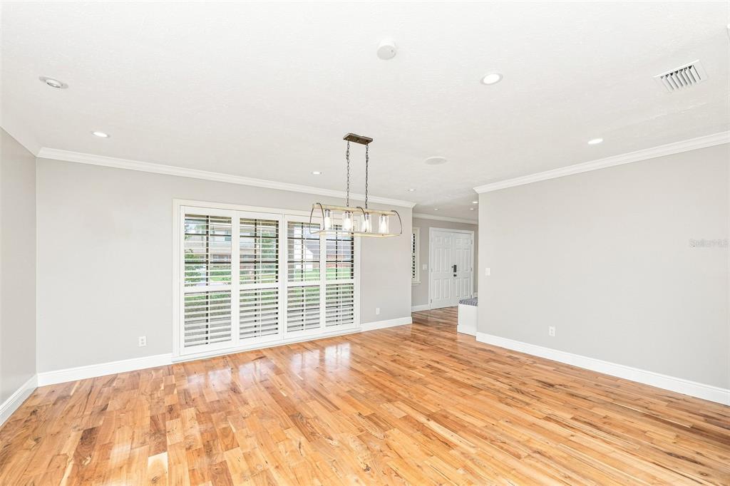An empty room features light gray walls, hardwood floors, a modern chandelier, and plantation shutters — 1010 MALLOW WAY, BRANDON, FL