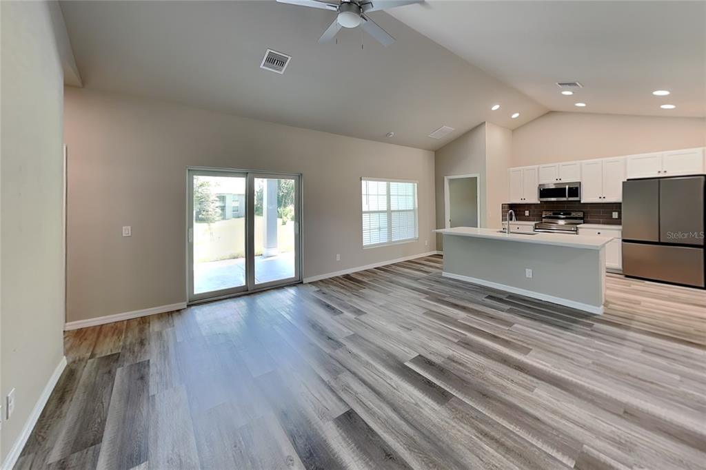 An open-concept living area features wood-look flooring, a kitchen island, and sliding glass patio doors — 8878 BESSEMER COURT, NORTH PORT, FL