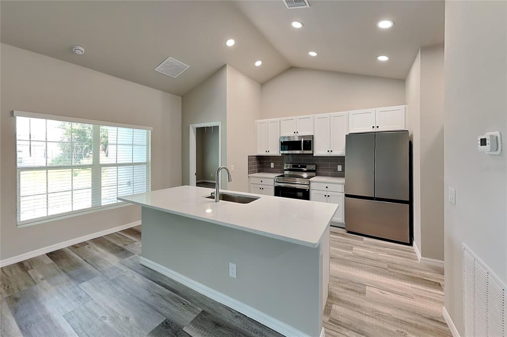 A modern kitchen features white cabinets, stainless steel appliances, a center island, and wood-look flooring — 8878 BESSEMER COURT, NORTH PORT, FL
