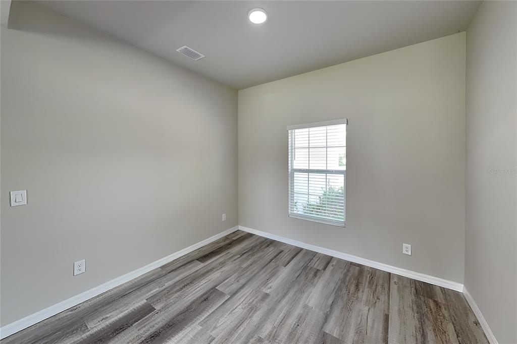An empty room features light-colored walls, wood-look flooring, a single window, and a ceiling light — 8878 BESSEMER COURT, NORTH PORT, FL