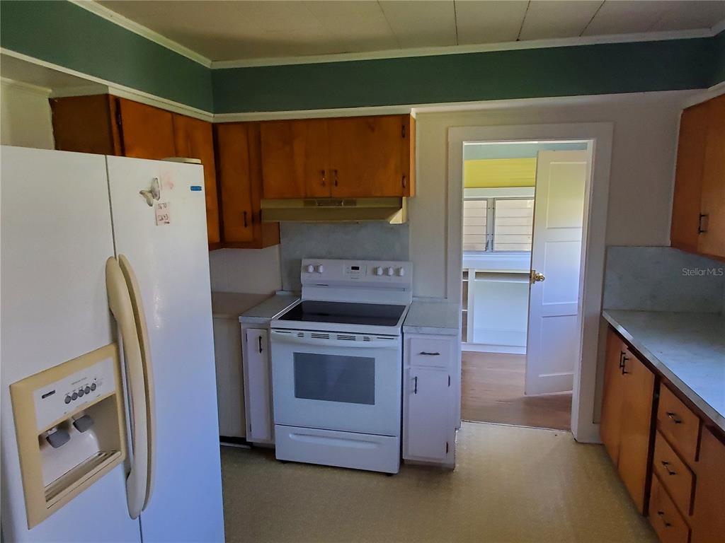 A kitchen features white appliances, wood cabinets, and a doorway leading to a sunroom — 18670 NW 246TH STREET, HIGH SPRINGS, FL