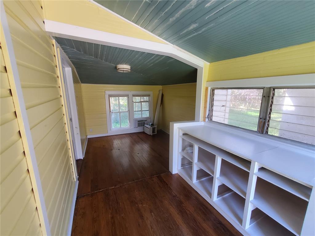 A sunroom with yellow walls, a blue ceiling, wood floors, and built-in white shelving — 18670 NW 246TH STREET, HIGH SPRINGS, FL