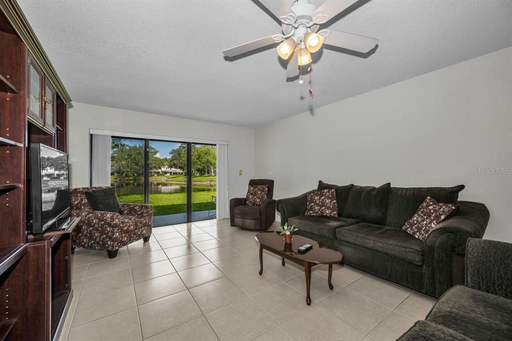 A living room with tile floors, a ceiling fan, and sliding glass doors overlooking a pond — 3505 TARPON WOODS BOULEVARD UNIT O-403, PALM HARBOR, FL