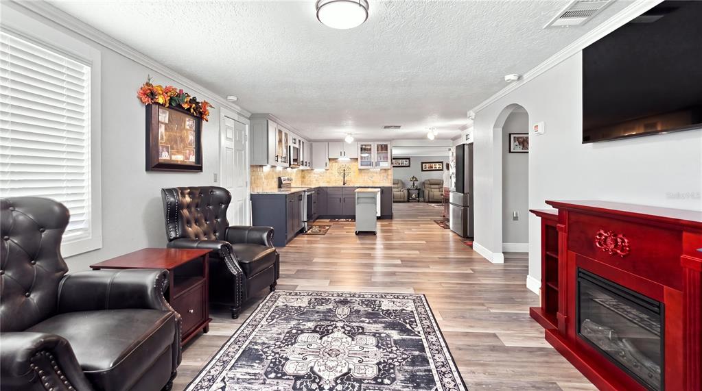 A living room with a fireplace and leather armchairs opens into a kitchen with gray cabinets — 14125 PLUM LANE, HUDSON, FL