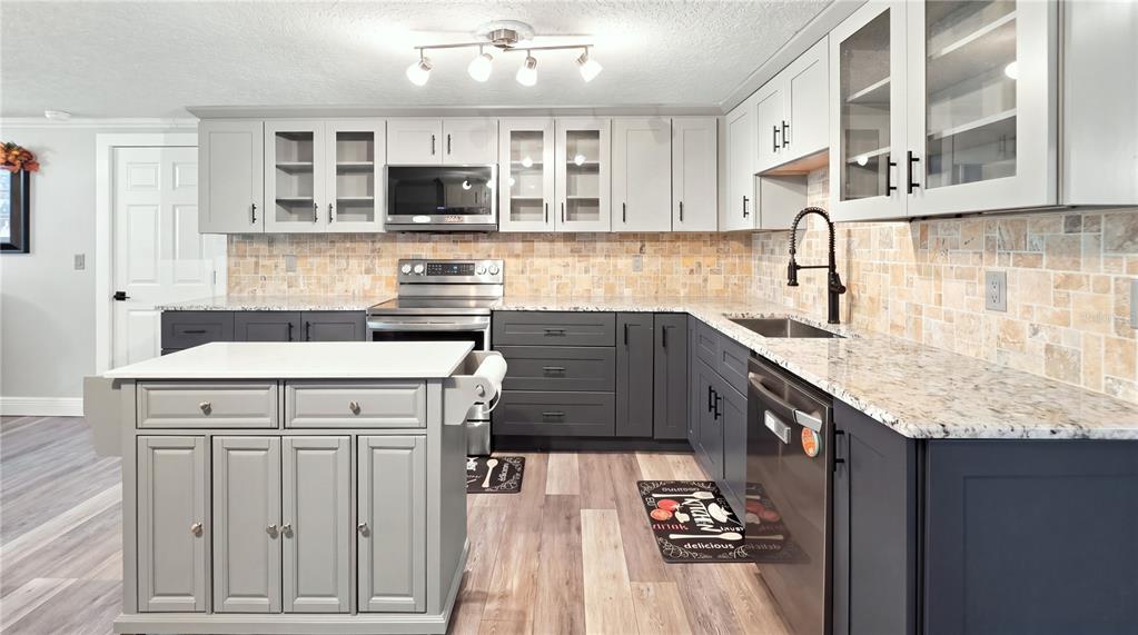 A kitchen features gray cabinetry, a central island, granite countertops, and a tiled backsplash — 14125 PLUM LANE, HUDSON, FL
