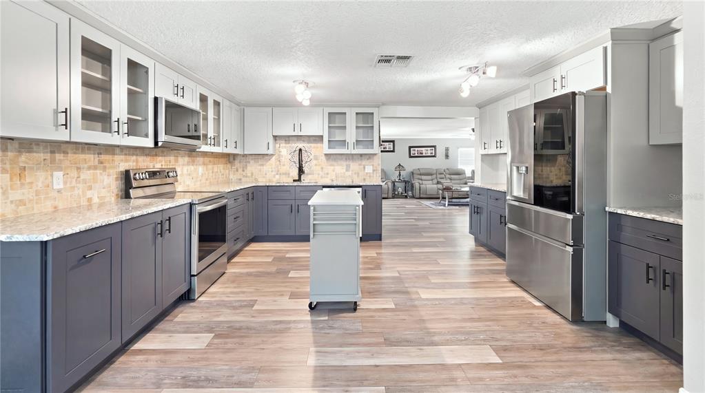 A kitchen features two-toned gray and white cabinetry, stainless steel appliances, and wood-look flooring — 14125 PLUM LANE, HUDSON, FL