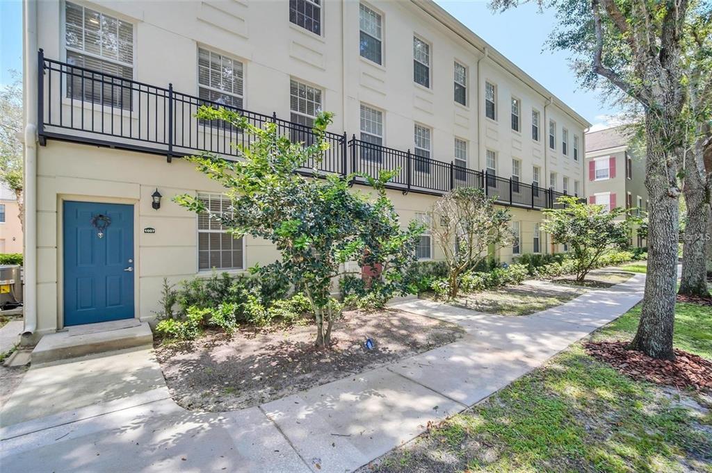 A three-story townhouse exterior with a blue front door, black railings, and a concrete walkway — 1007 SIENA PARK BOULEVARD E, KISSIMMEE, FL