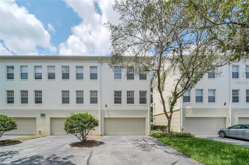 A three-story townhouse exterior features a beige stucco facade, multiple windows, and three garage doors — 1007 SIENA PARK BOULEVARD E, KISSIMMEE, FL