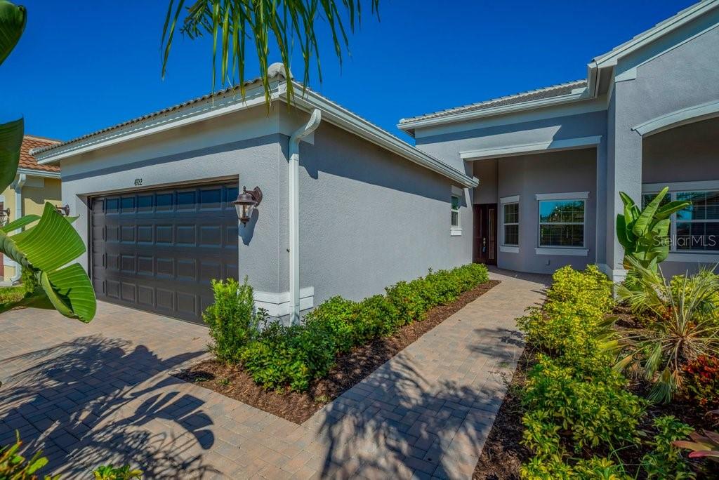 A gray stucco house features a dark garage door and a paved walkway leading to the entrance — 4922 SIENNA ISLES AVENUE, WIMAUMA, FL