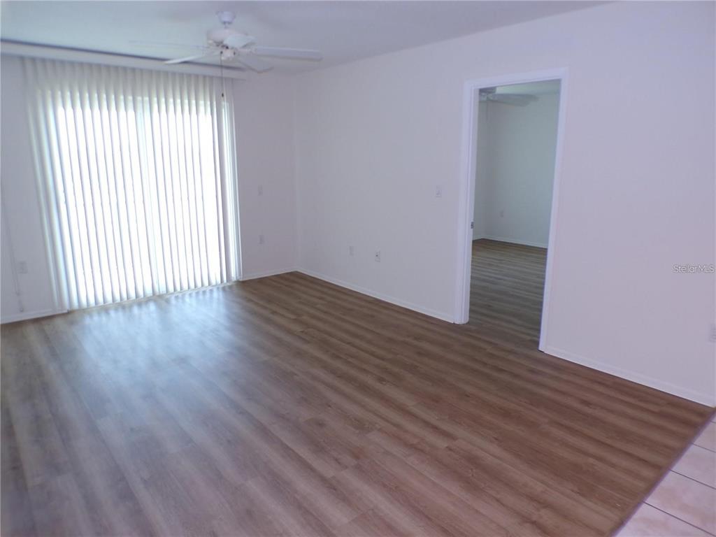 An empty living room features wood-look flooring, a ceiling fan, and sliding glass patio doors — 649 S TAMIAMI TRAIL S UNIT 304, VENICE, FL