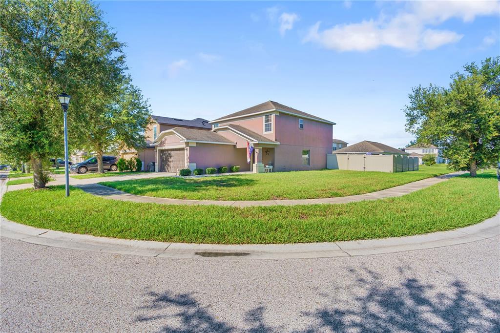 A two-story house with a tan stucco exterior sits on a corner lot with a lawn — 7719 MAROON PEAK DRIVE, RUSKIN, FL