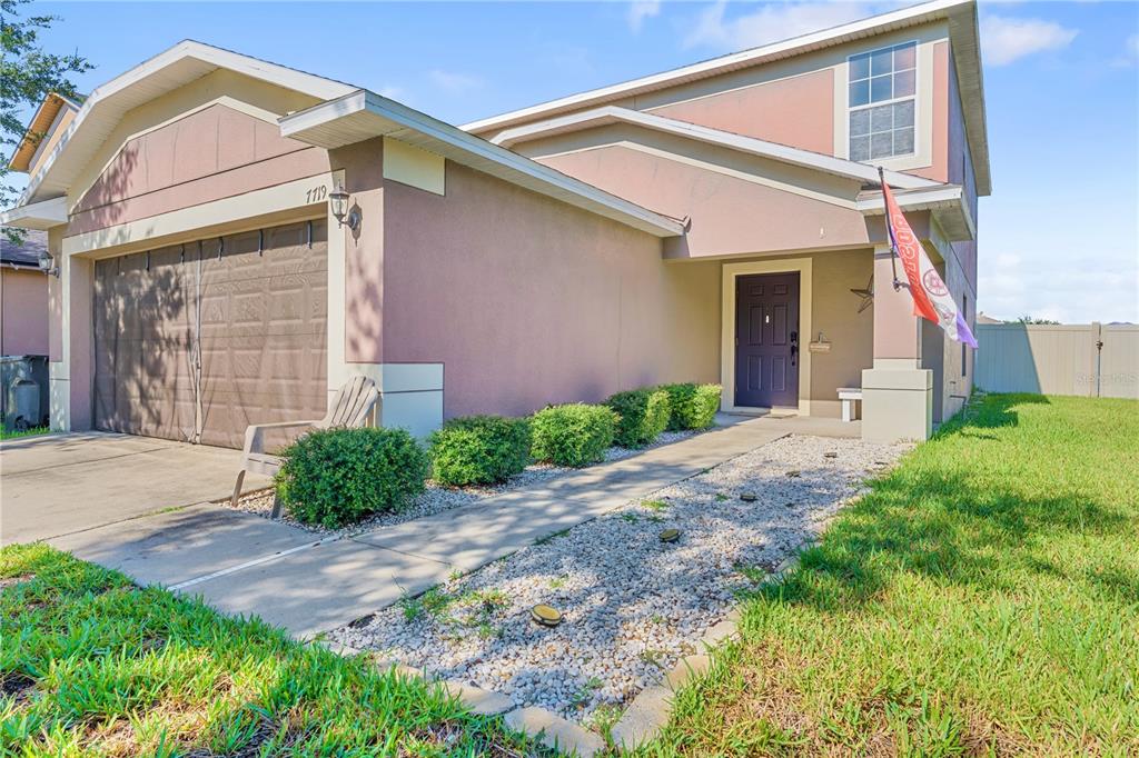 A two-story house features a garage, a gravel walkway, and a front door with a flag — 7719 MAROON PEAK DRIVE, RUSKIN, FL