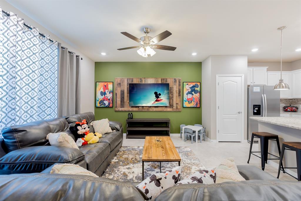 A living room features a green accent wall with a television, gray sofa, and kitchen — 7581 OAK SPRING LANE, DAVENPORT, FL