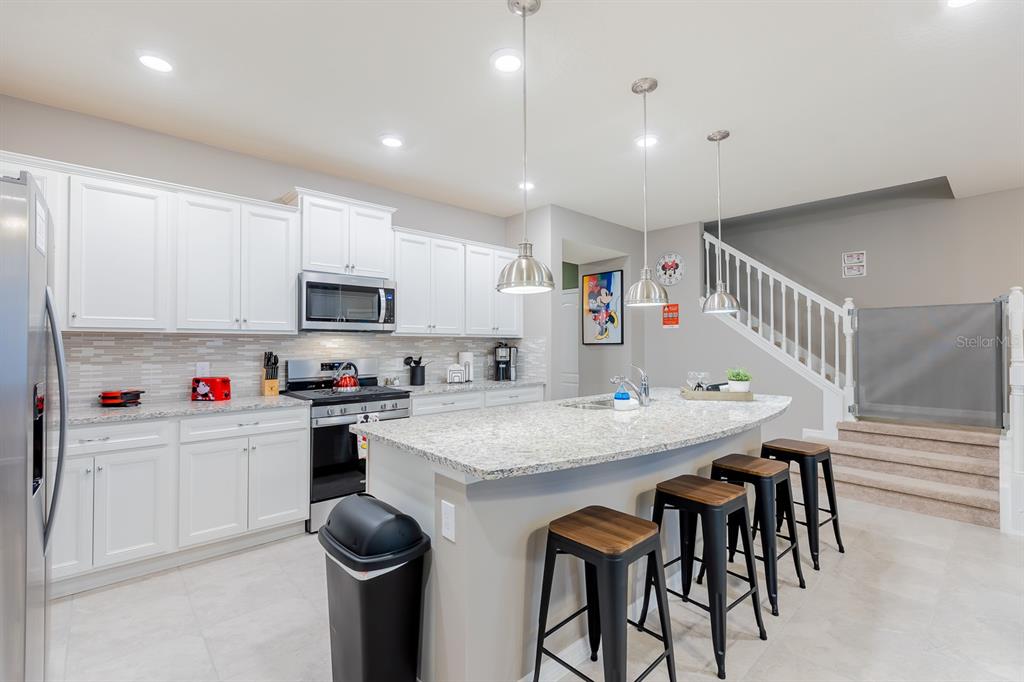 A kitchen features white cabinets, granite countertops, a central island with bar stools, and stairs — 7581 OAK SPRING LANE, DAVENPORT, FL