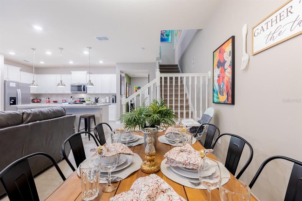 A dining area with a wooden table leads into an open kitchen with white cabinets — 7581 OAK SPRING LANE, DAVENPORT, FL