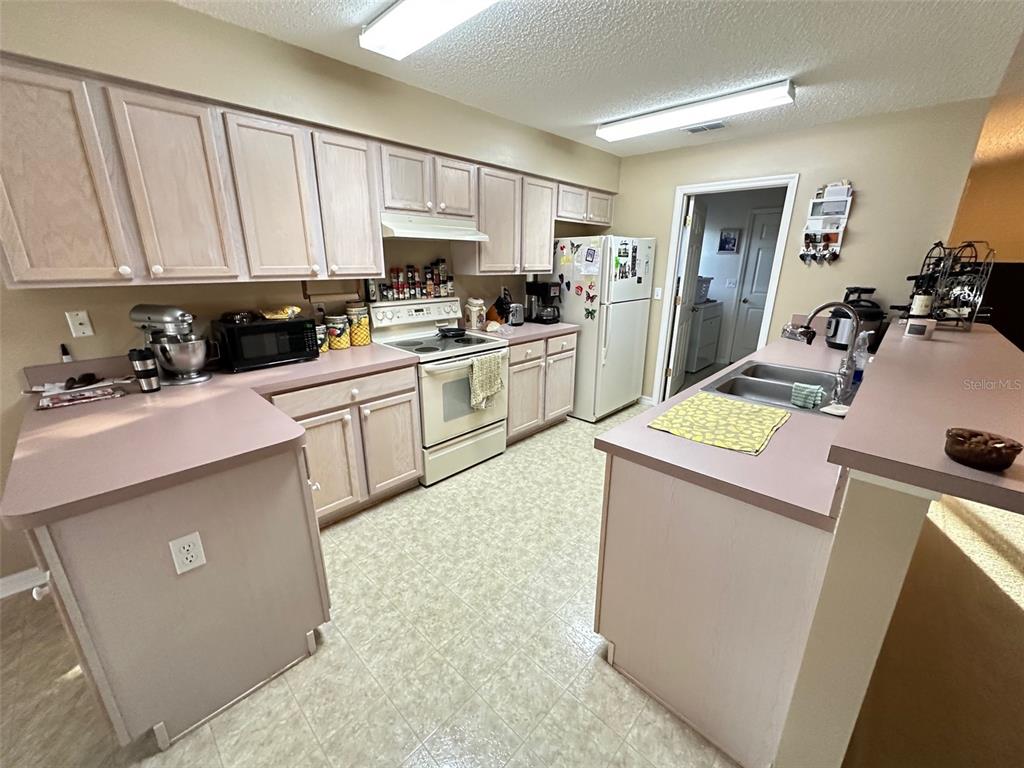 A kitchen features light wood cabinets, laminate countertops, white appliances, and a double sink — 32905 TIMBERWOOD DRIVE, LEESBURG, FL