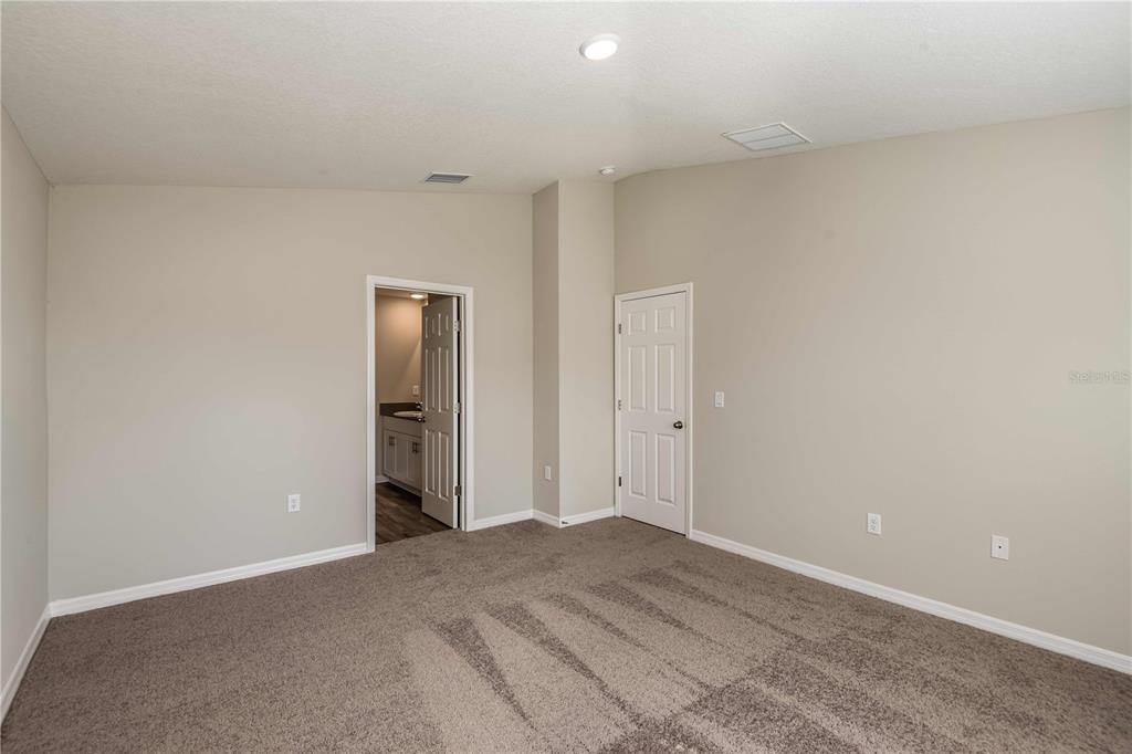 An empty bedroom with beige walls, gray carpeting, a doorway to a bathroom, and a closet — 1362 PALMEROY ROAD, HAINES CITY, FL