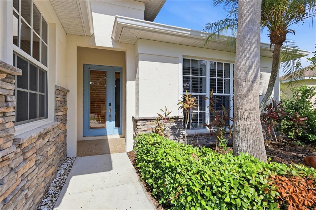 A light blue front door is set in a stucco home with stone veneer accents — 310 SALVIA COURT, BRADENTON, FL