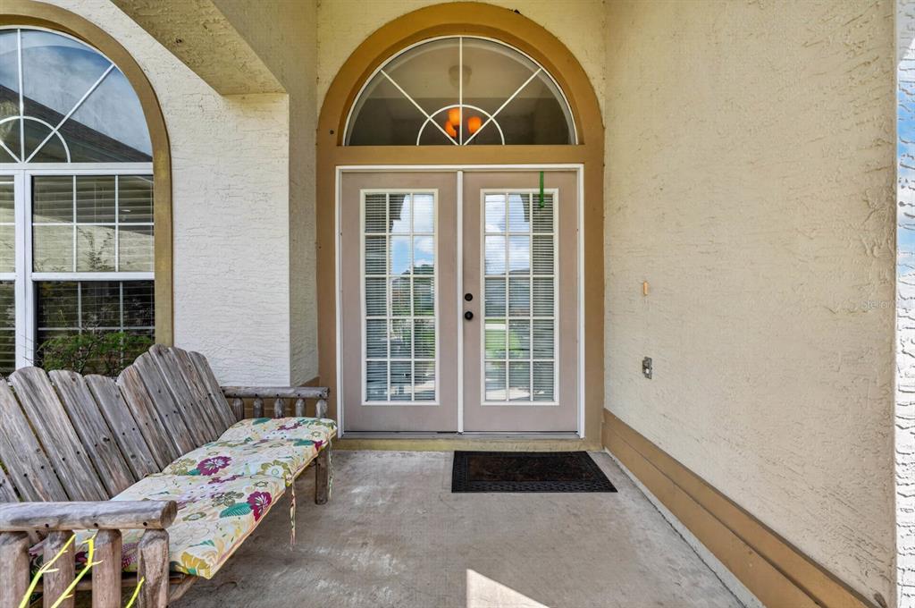 A covered front porch features a wooden bench, double glass-paneled doors, and an arched transom window — 25 KATHRYN PLACE, PALM COAST, FL
