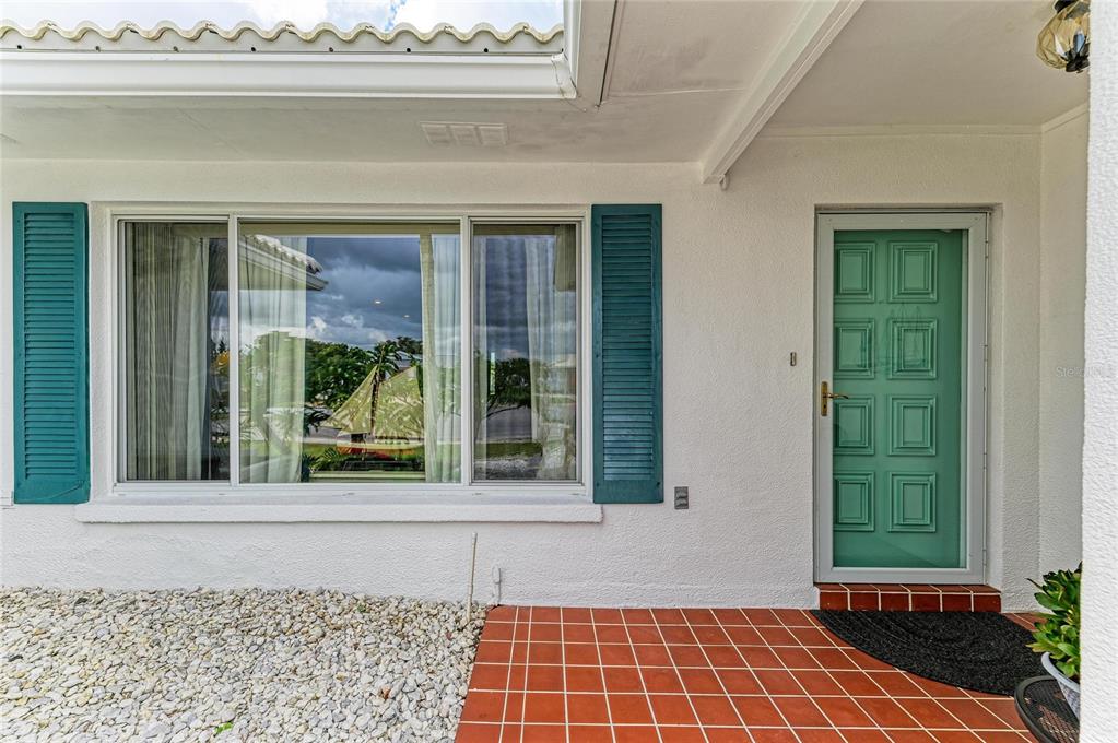 A teal front door and matching shutters accent the white exterior of this home entrance — 4006 JOYCE DRIVE, BRADENTON, FL
