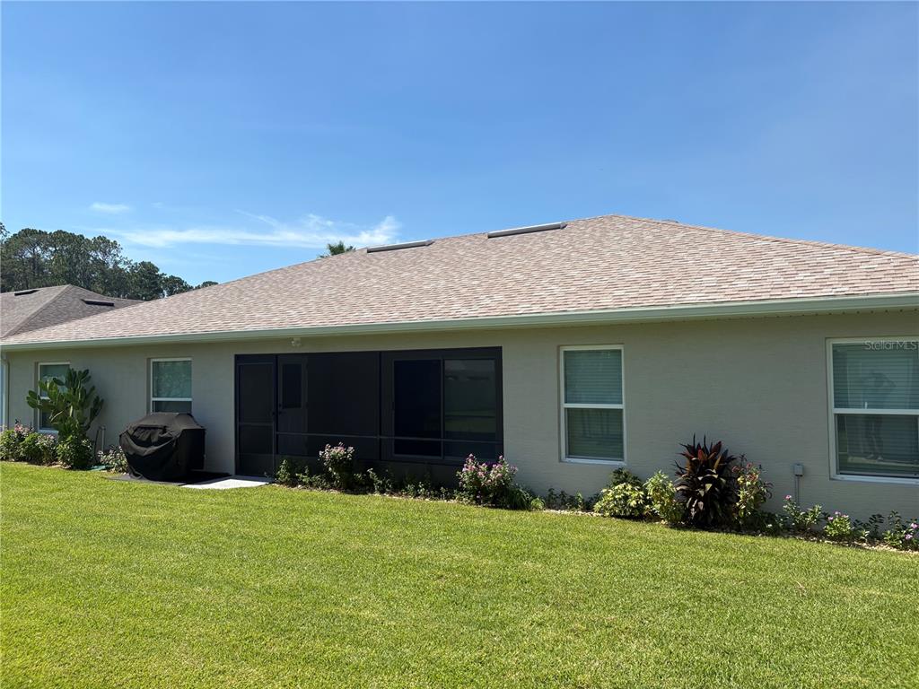 The rear exterior of a single-story house features a screened-in porch and a grassy yard — 53 ERIC DRIVE, PALM COAST, FL