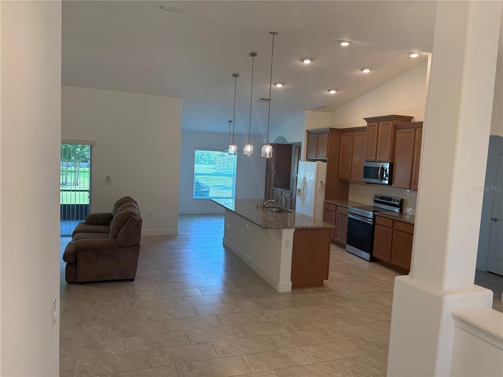 An open-concept kitchen features granite countertops, wood cabinets, and stainless steel appliances — 53 ERIC DRIVE, PALM COAST, FL