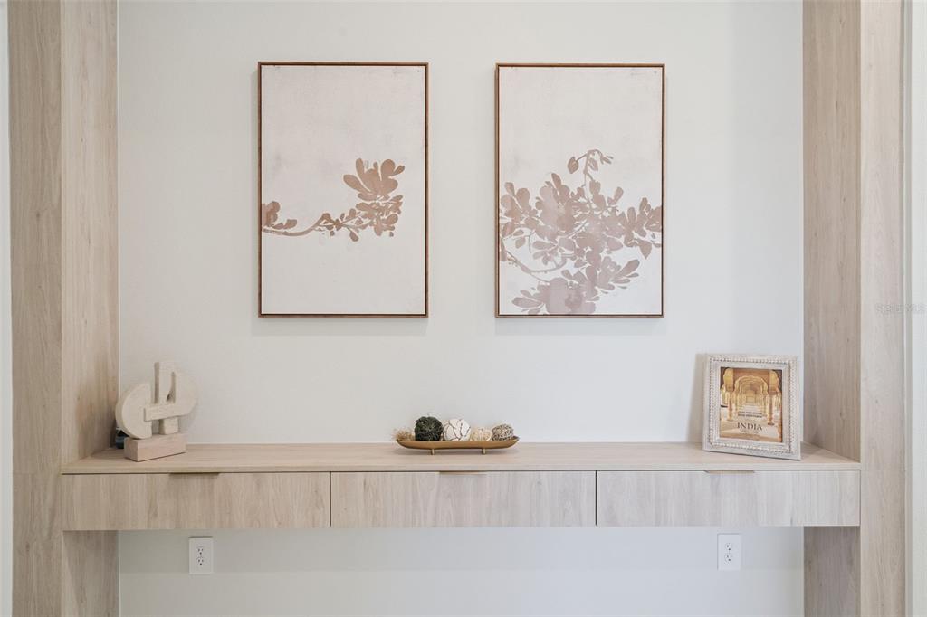 A light wood built-in console table sits below two framed floral art pieces on a wall — 419 SKYFIELD COURT, LADY LAKE, FL