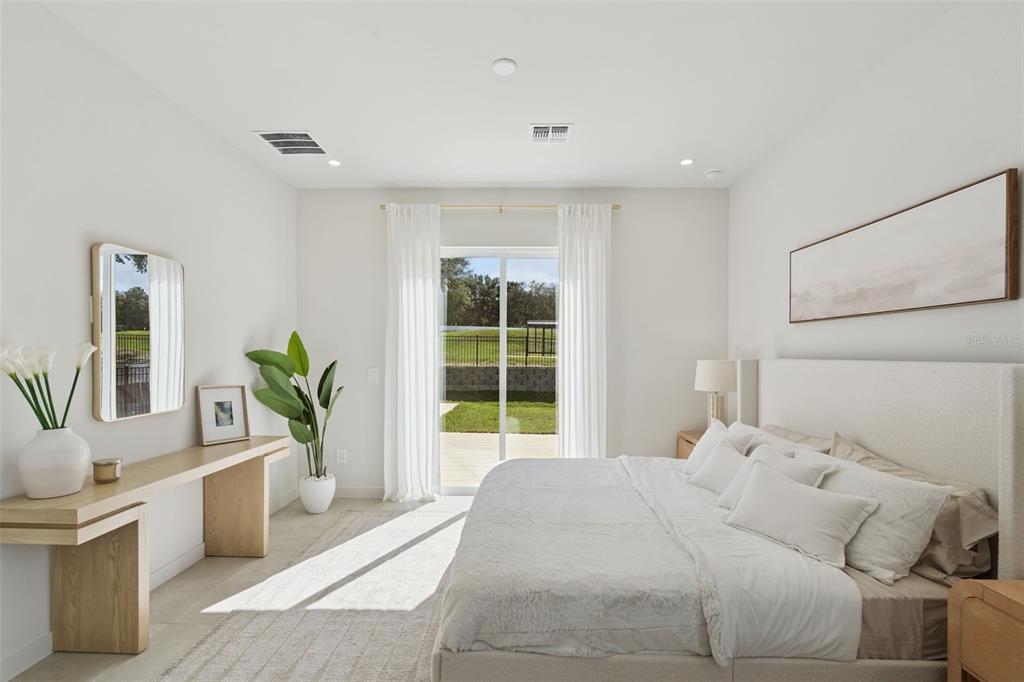 A bright bedroom features a king bed, light wood console table, and sliding glass patio doors — 419 SKYFIELD COURT, LADY LAKE, FL