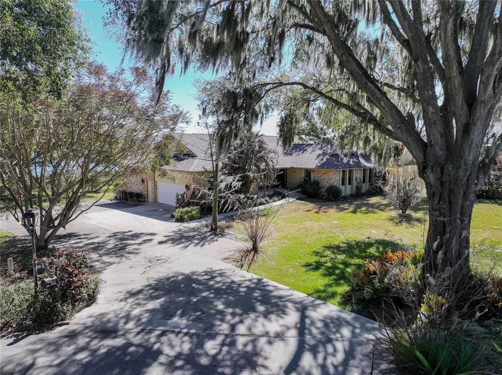 A single-story house with a stone facade and a driveway sits among large trees — 13 HERMOSA DRIVE, EUSTIS, FL