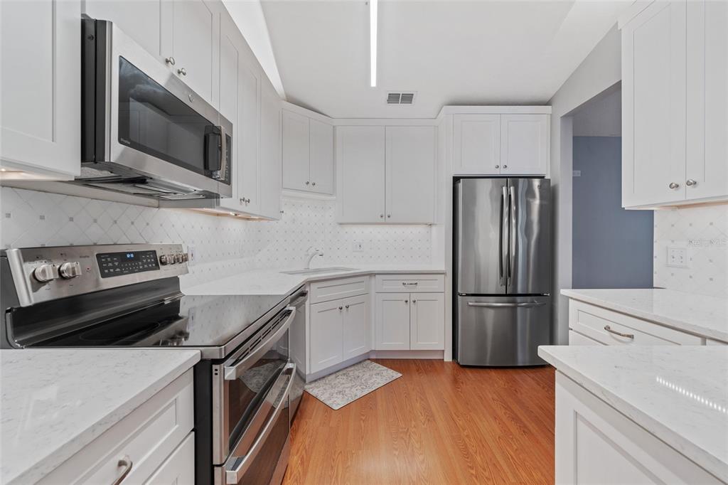 A kitchen features white cabinets, stainless steel appliances, quartz countertops, and hardwood flooring — 1010 LOCH VAIL UNIT 23, APOPKA, FL