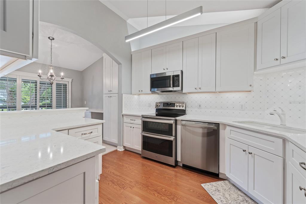 A kitchen features white cabinets, stainless steel appliances, quartz countertops, and hardwood flooring — 1010 LOCH VAIL UNIT 23, APOPKA, FL