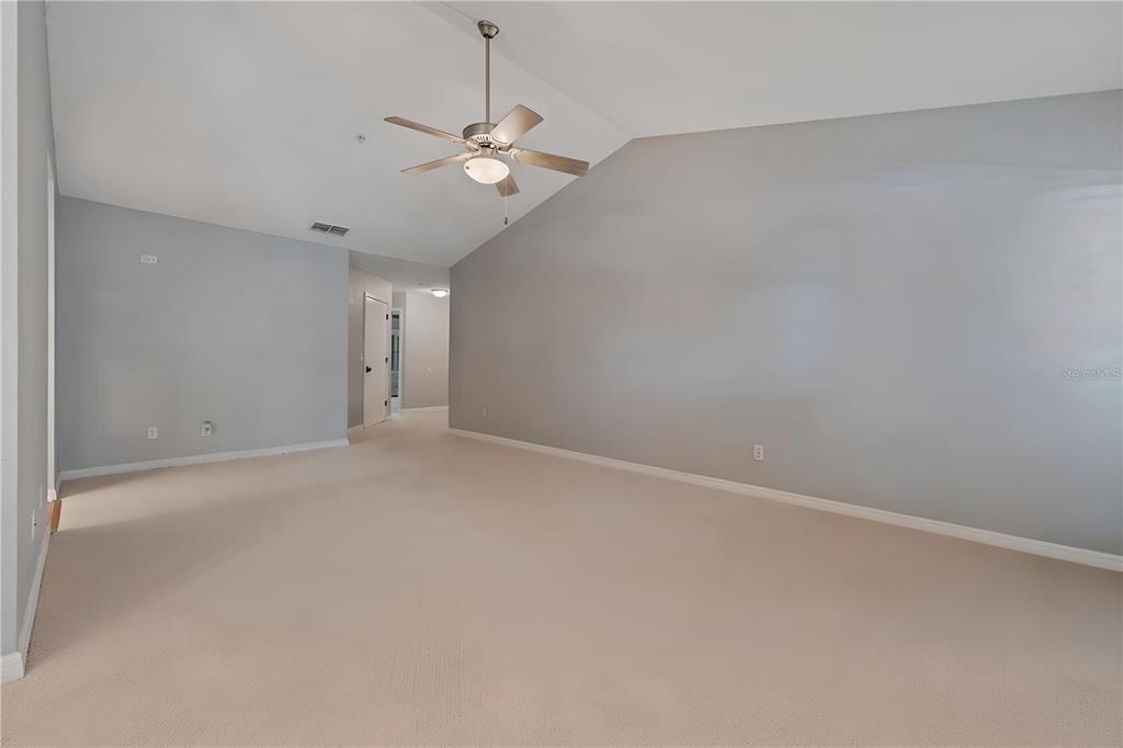 An empty living room features light gray walls, beige carpeting, and a vaulted ceiling — 1010 LOCH VAIL UNIT 23, APOPKA, FL