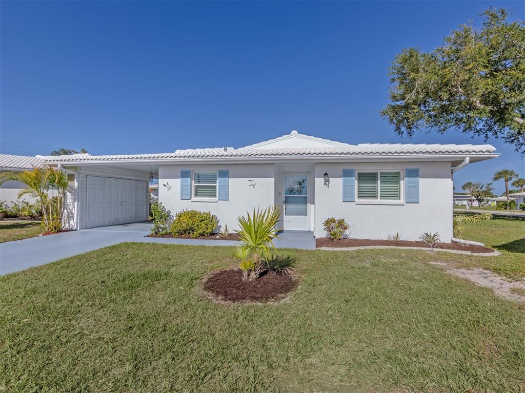 A white, single-story house with a carport, blue shutters, and a front lawn — 414 CIRCLEWOOD DRIVE UNIT H2, VENICE, FL