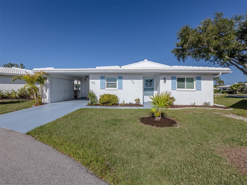 A single-story white house with a carport, blue shutters, and a front lawn — 414 CIRCLEWOOD DRIVE UNIT H2, VENICE, FL