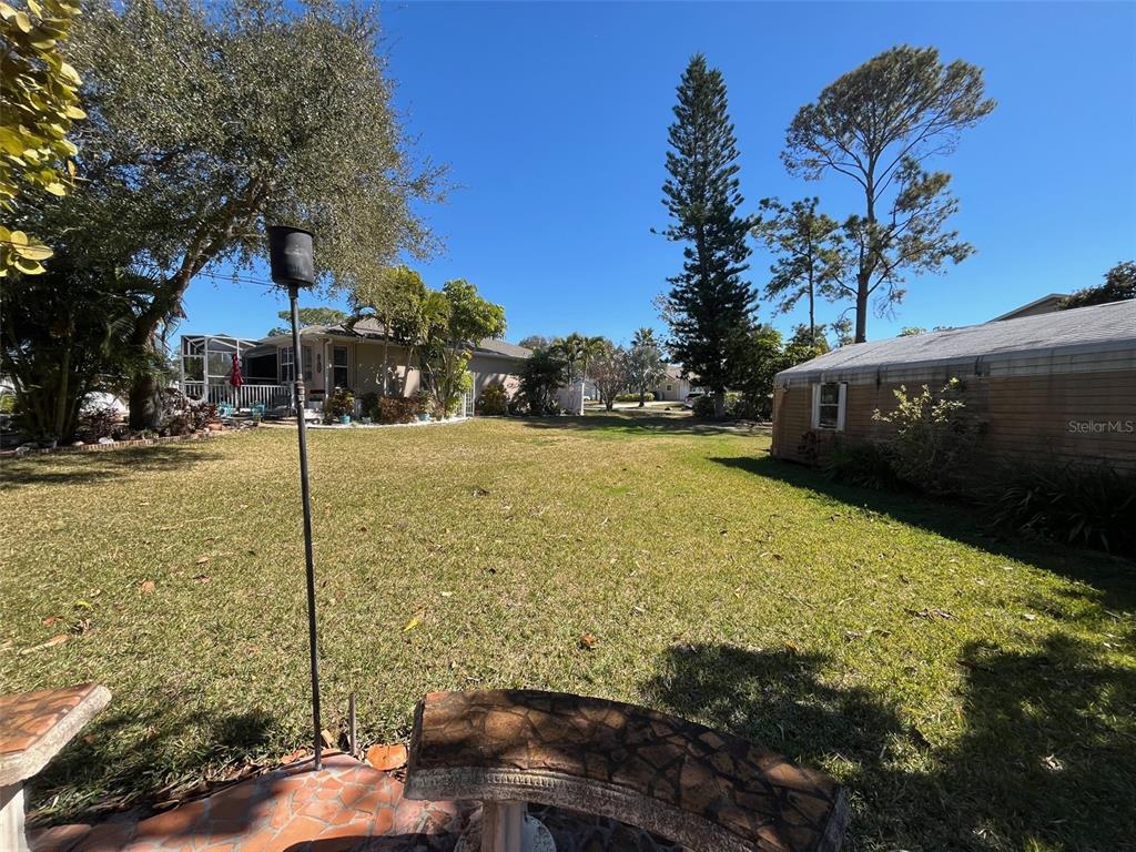 A grassy backyard features a stone bench, a bird feeder, and neighboring houses — Lot 96 BLUE JAY CIRCLE, PALM HARBOR, FL