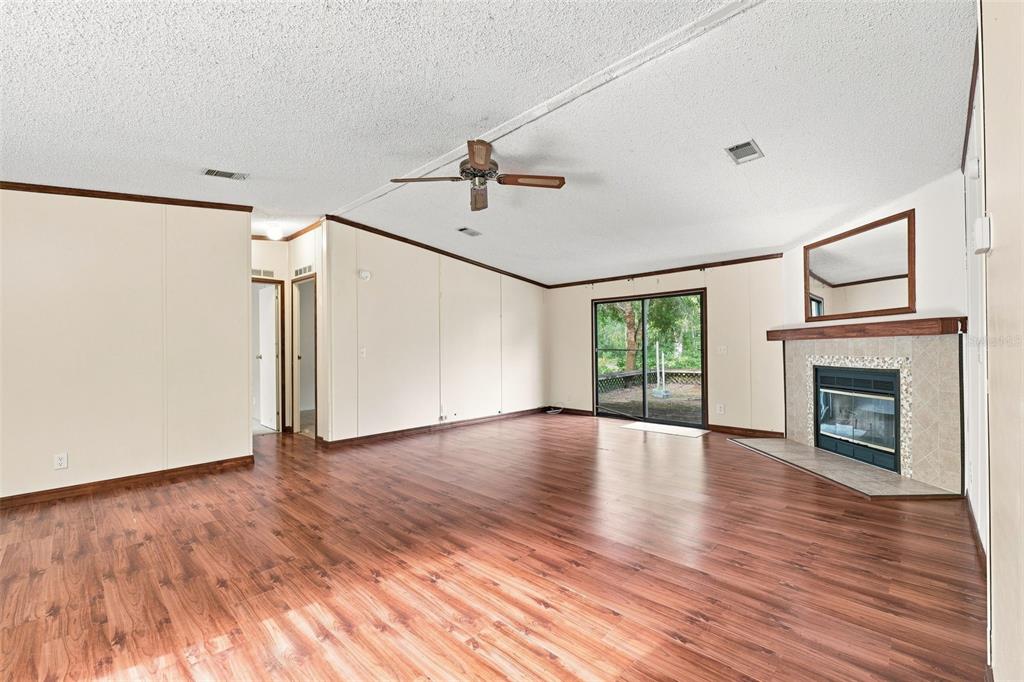 A living room with wood-look flooring, a fireplace, a ceiling fan, and sliding glass doors — 4311 CULBREATH ROAD, BROOKSVILLE, FL
