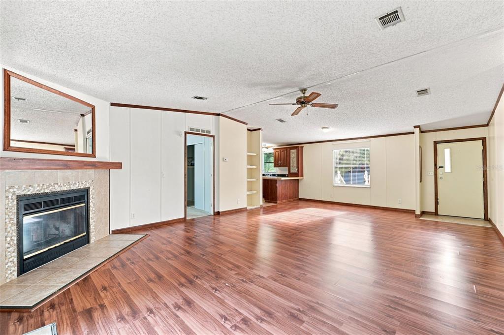 A spacious living room features wood-look flooring, a fireplace, a ceiling fan, and an open kitchen — 4311 CULBREATH ROAD, BROOKSVILLE, FL