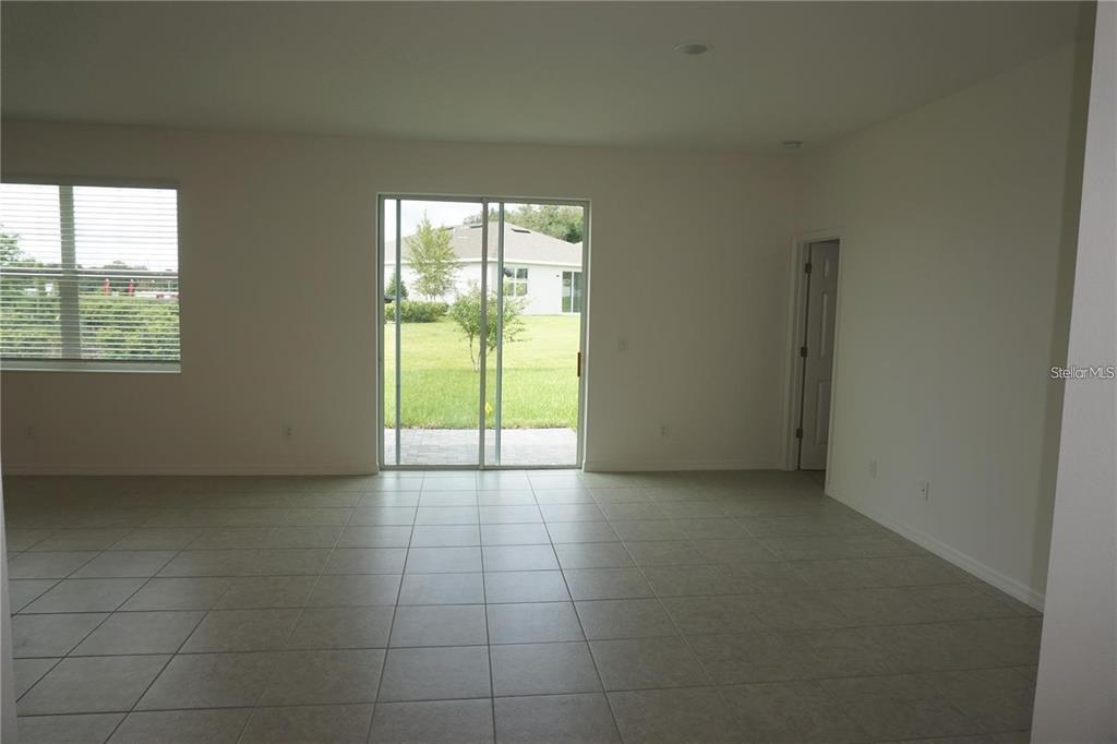 An empty room with light-colored tile flooring, a sliding glass door, and a single window — 1677 WAY OF PEACE LANE, MASCOTTE, FL