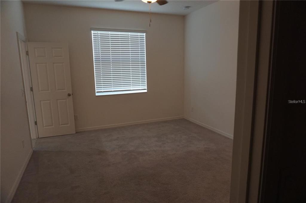 An empty bedroom features beige walls, gray carpeting, a ceiling fan, and a window with blinds — 1677 WAY OF PEACE LANE, MASCOTTE, FL