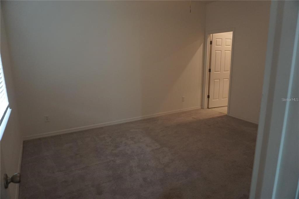 An empty bedroom with beige carpet, white walls, and a doorway leading to another room — 1677 WAY OF PEACE LANE, MASCOTTE, FL