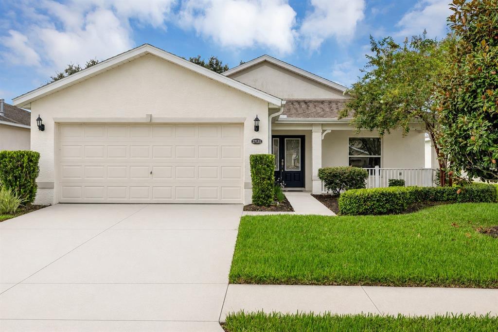 A single-story house with a beige stucco exterior, a two-car garage, and a front porch — 27131 ROANOKE DRIVE, LEESBURG, FL