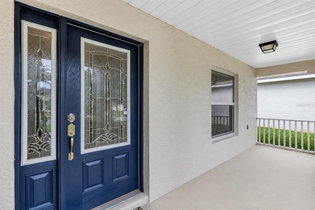 A blue front door with decorative glass panels sits on a covered porch with stucco walls — 27131 ROANOKE DRIVE, LEESBURG, FL