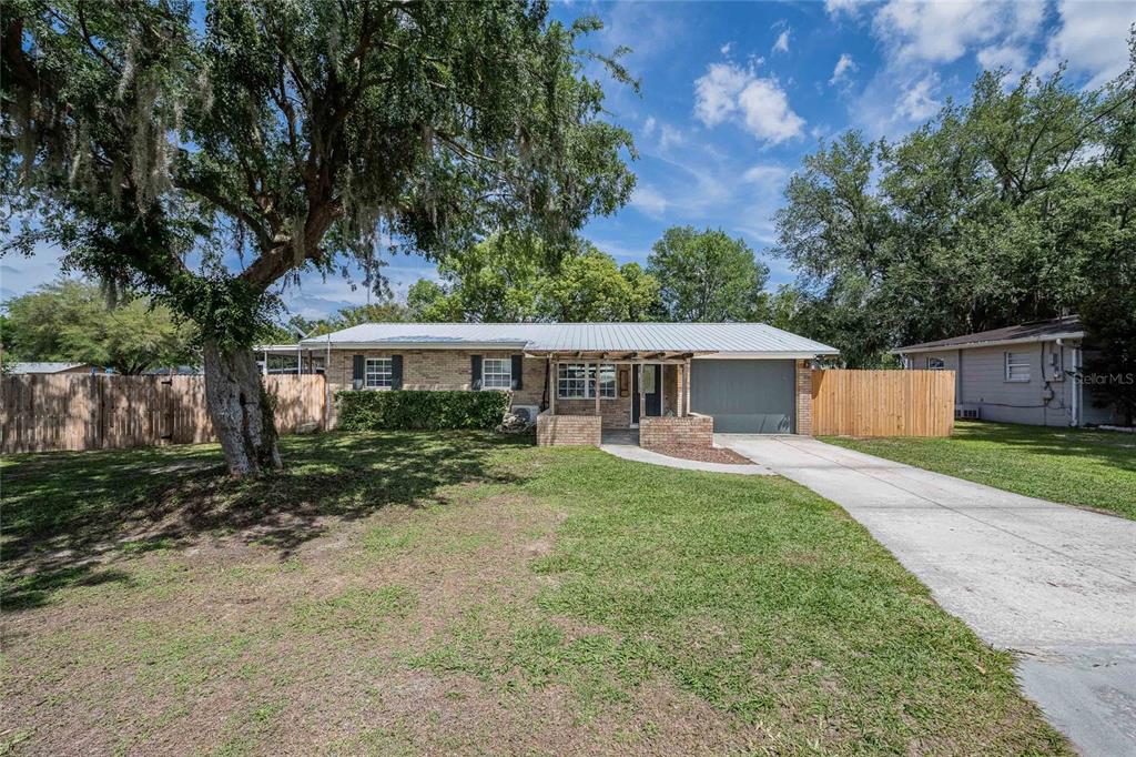 A single-story brick house with a metal roof, attached garage, and a large front tree — 218 MAPLE LANE, FORT MEADE, FL