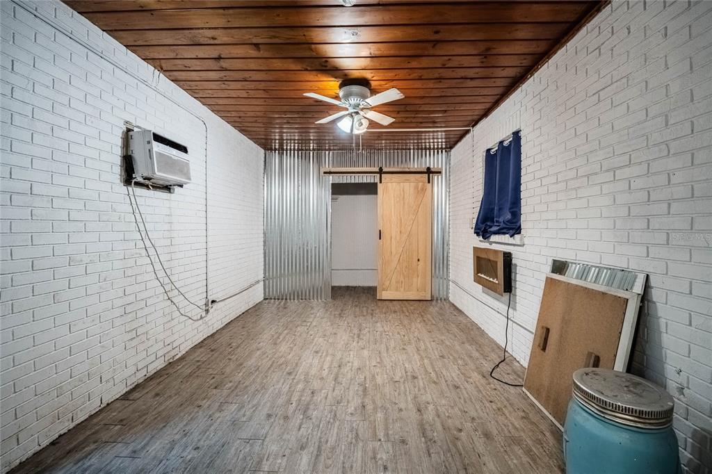 A room with white brick walls, a wood-plank ceiling, wood-look flooring, and a sliding barn door — 218 MAPLE LANE, FORT MEADE, FL
