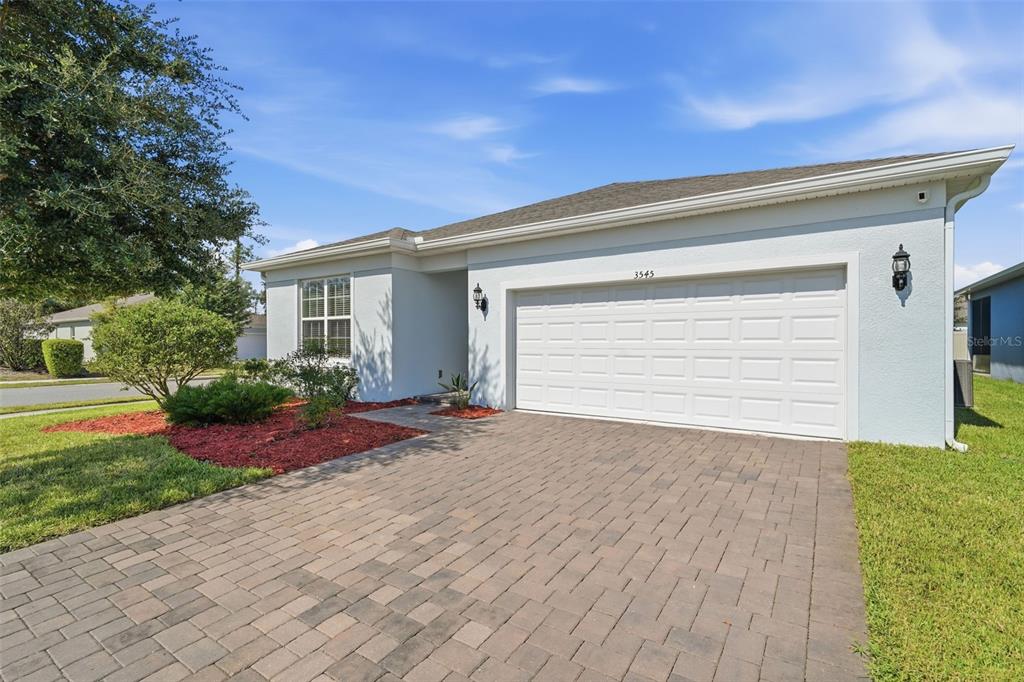 A single-story house with a white stucco exterior, a two-car garage, and a paver driveway — 3545 TREETOP STREET, DELAND, FL