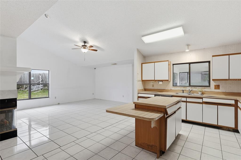 A kitchen features white cabinets, wood-trimmed laminate countertops, a central island, and white tile flooring — 2939 DANFORTH DRIVE, ORLANDO, FL