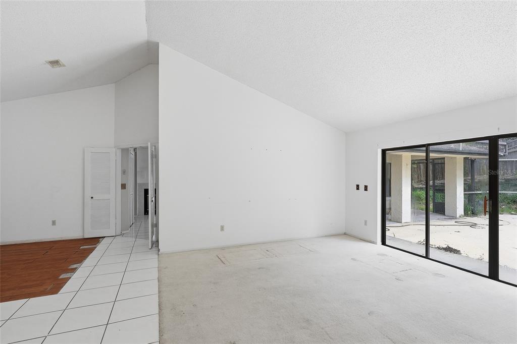 An open-concept living room and kitchen featuring white tile floors, a fireplace, and vaulted ceilings — 2939 DANFORTH DRIVE, ORLANDO, FL
