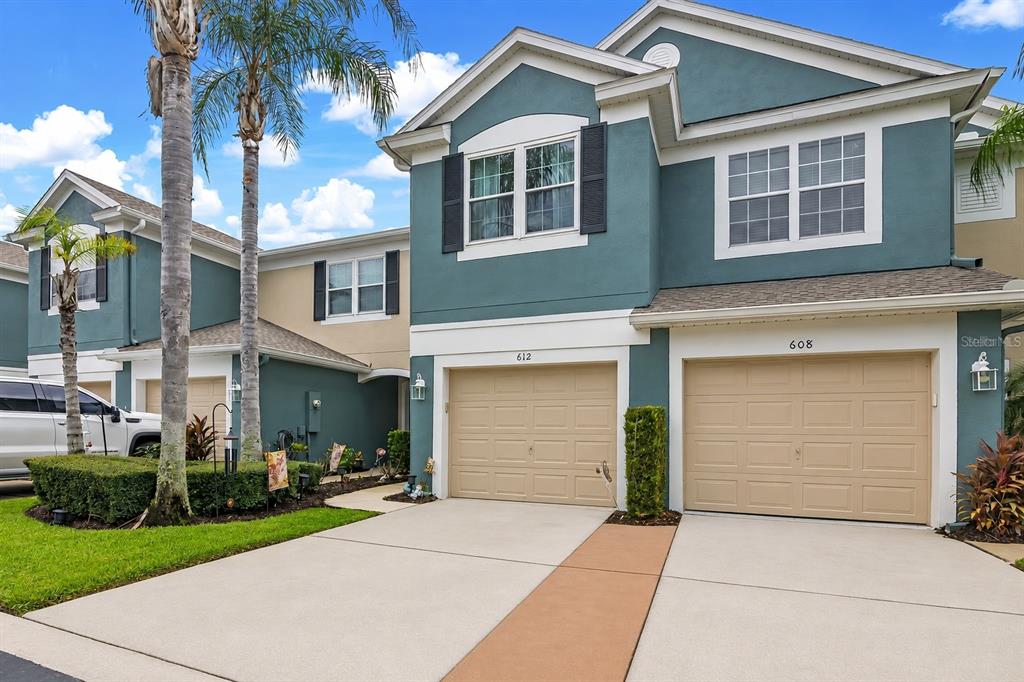 A two-story townhouse exterior with teal siding, two beige garage doors, and a concrete driveway — 612 SHROPSHIRE LOOP, SANFORD, FL