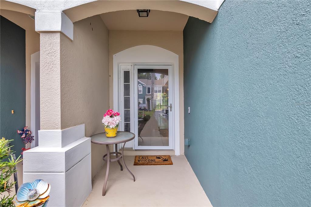 A covered entryway features a glass storm door, a small round table, and a welcome mat — 612 SHROPSHIRE LOOP, SANFORD, FL