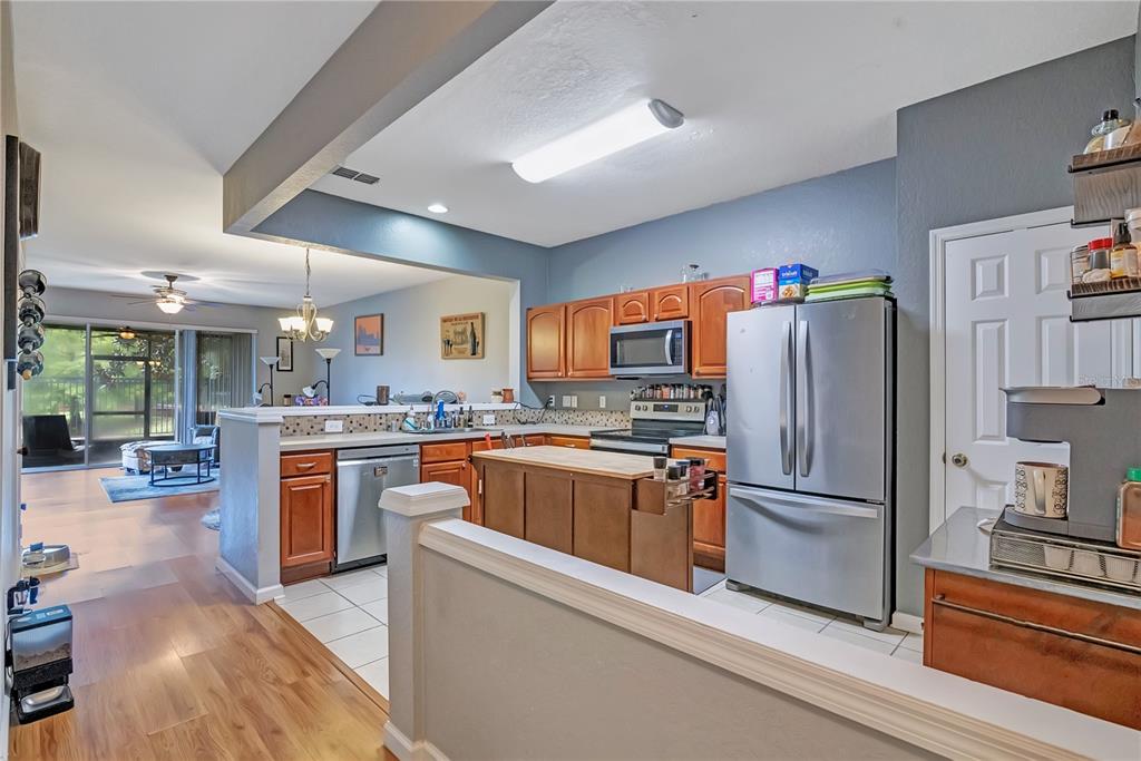A kitchen with wood cabinets, stainless steel appliances, and an island overlooks an adjacent living area — 612 SHROPSHIRE LOOP, SANFORD, FL